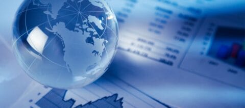 Blue shaded image of a glass globe of the world sitting on printed paperts of financial graphs and numbers.