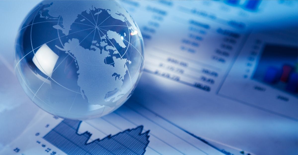 Blue shaded image of a glass globe of the world sitting on printed paperts of financial graphs and numbers.