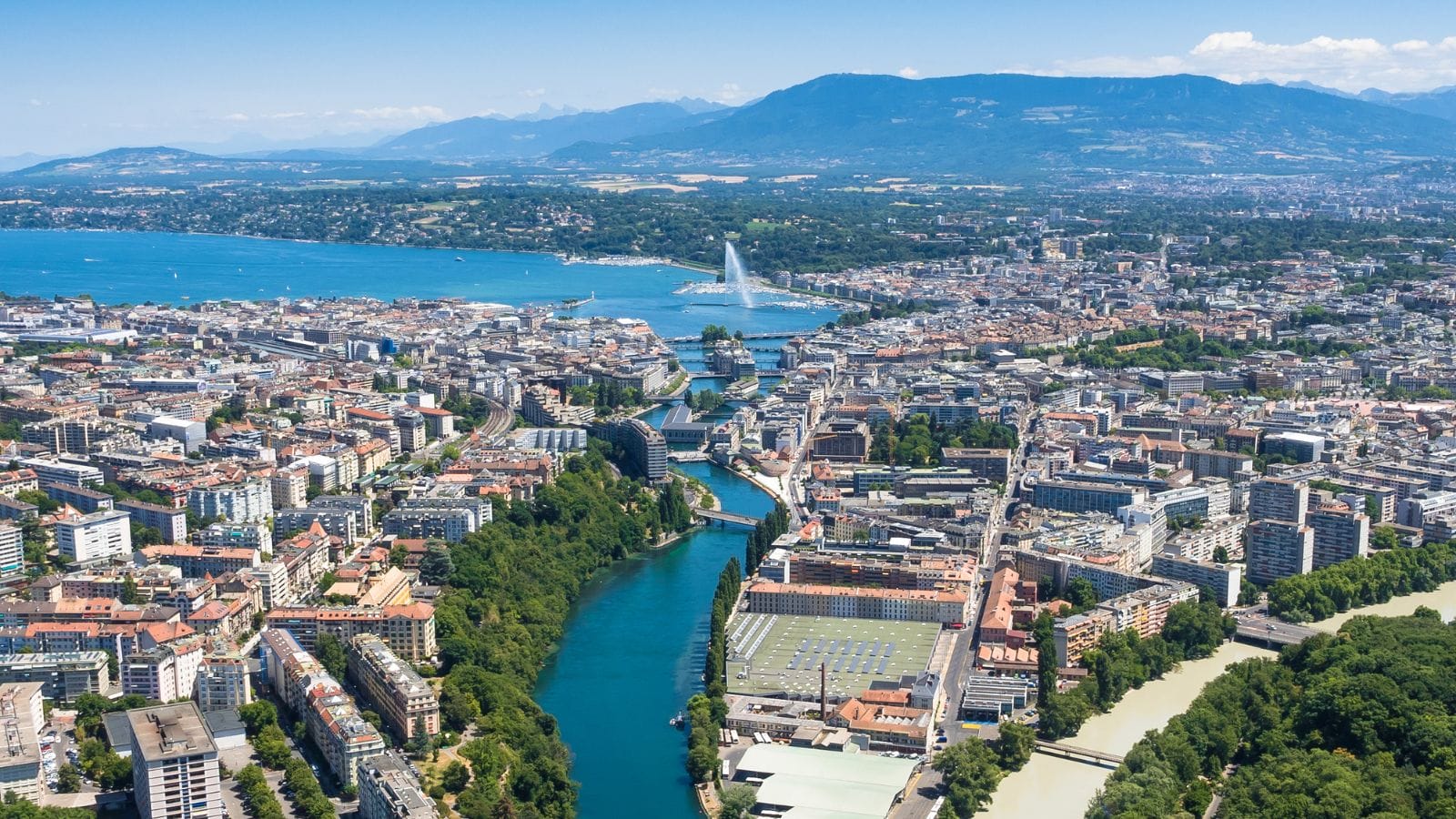 Rooftop view of sunny Geneva with lake Geneva and its fountain in the background.